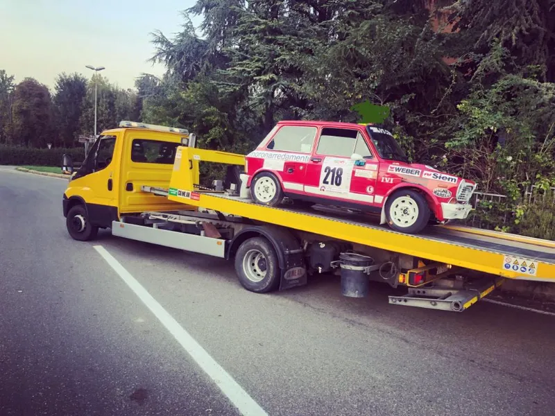 Carro attrezzi giallo che trasporta un'auto da rally bianca e rossa