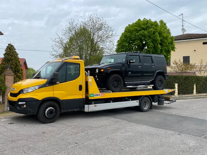 Carro attrezzi giallo con pianale che trasporta un fuoristrada nero