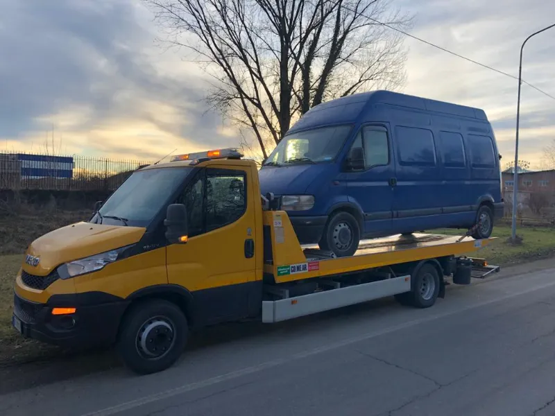 Carro attrezzi giallo con pianale che trasporta un furgone blu