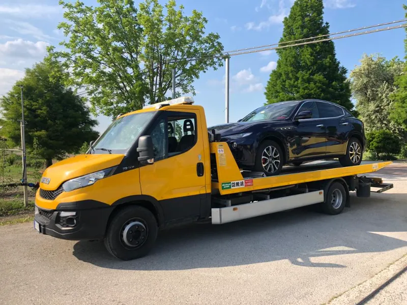 Carro attrezzi giallo con pianale che trasporta un SUV blu scuro